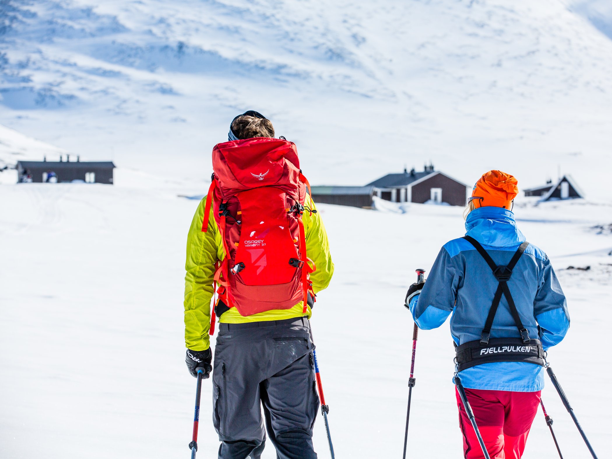 Two skiers on their way to a small brown mountain cabin.