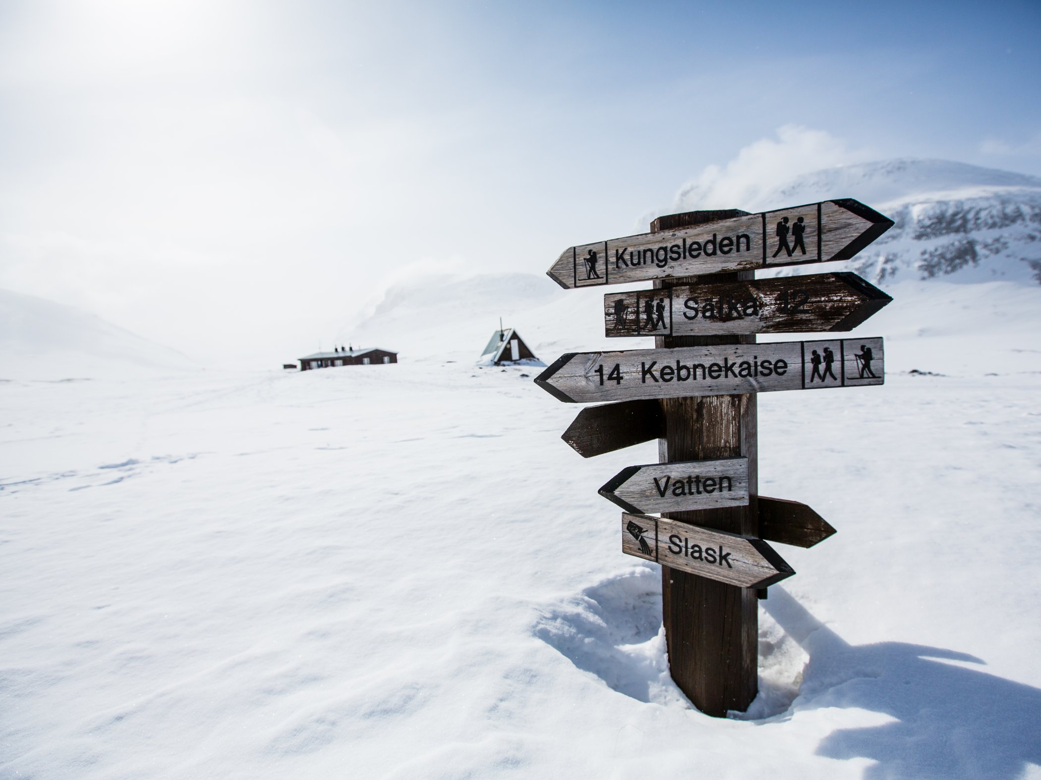 A sign with many arrows in wood showing directions and distances on the Kungsleden in winter.