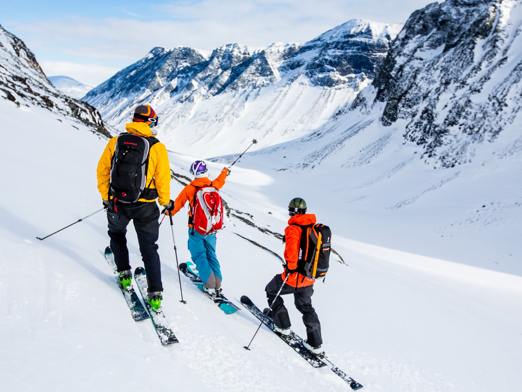 Three skiers on a ski touring route through a snow-covered mountain landscape.