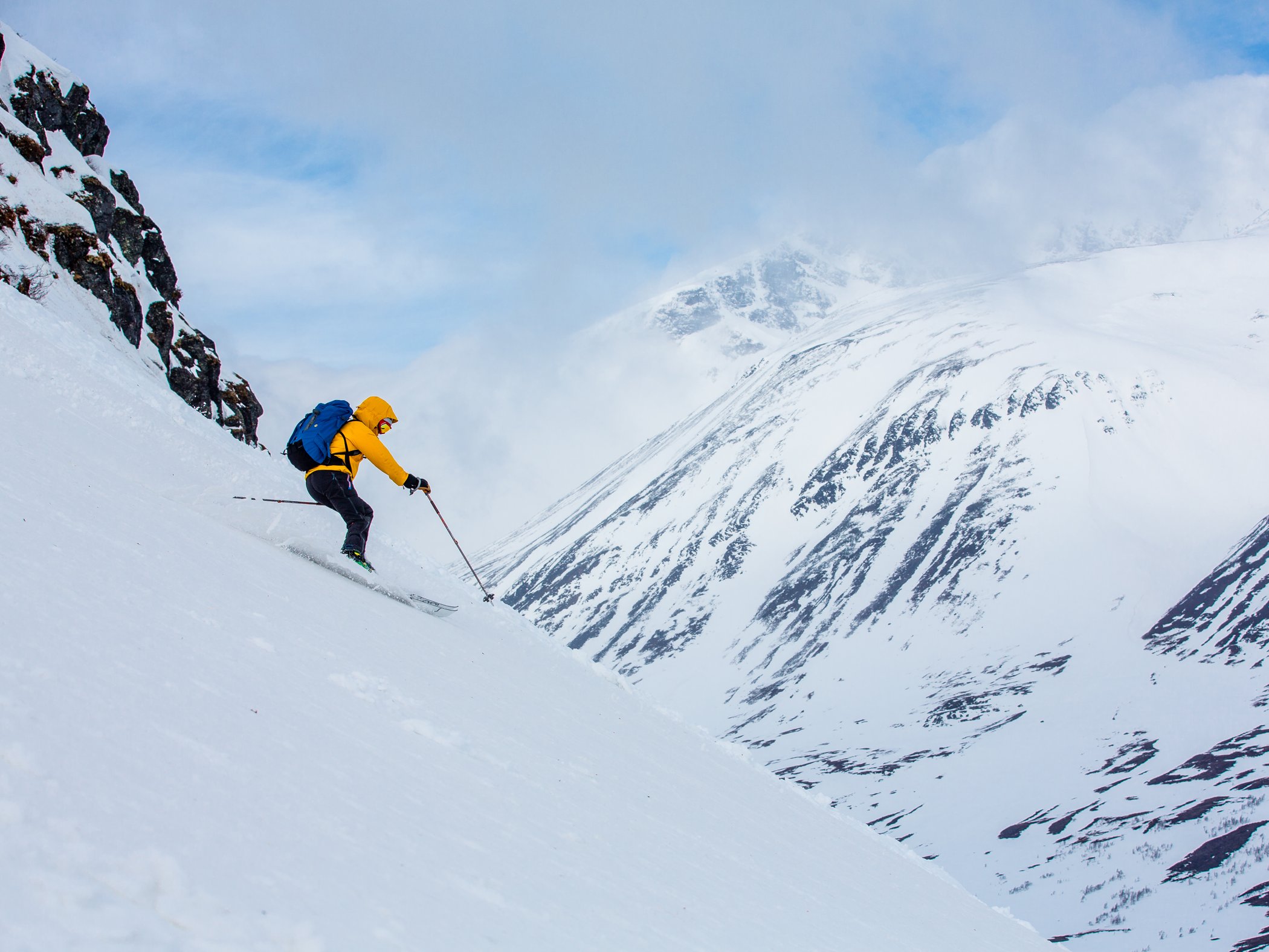 Skier descending a steep snowy mountain slope in a high alpine landscape.