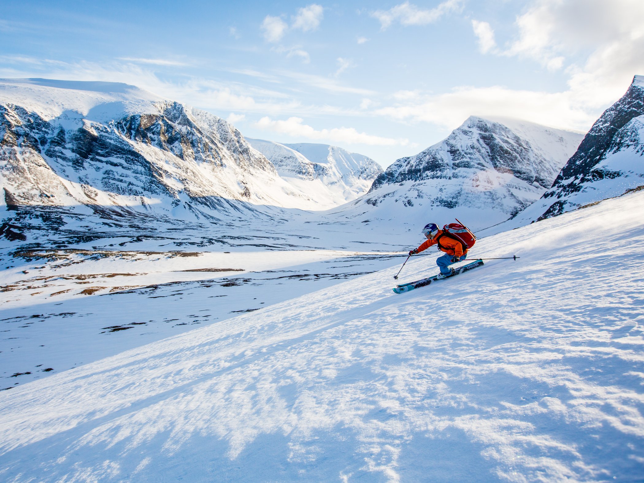 Skier descending a snowy mountain slope surrounded by rugged alpine peaks.