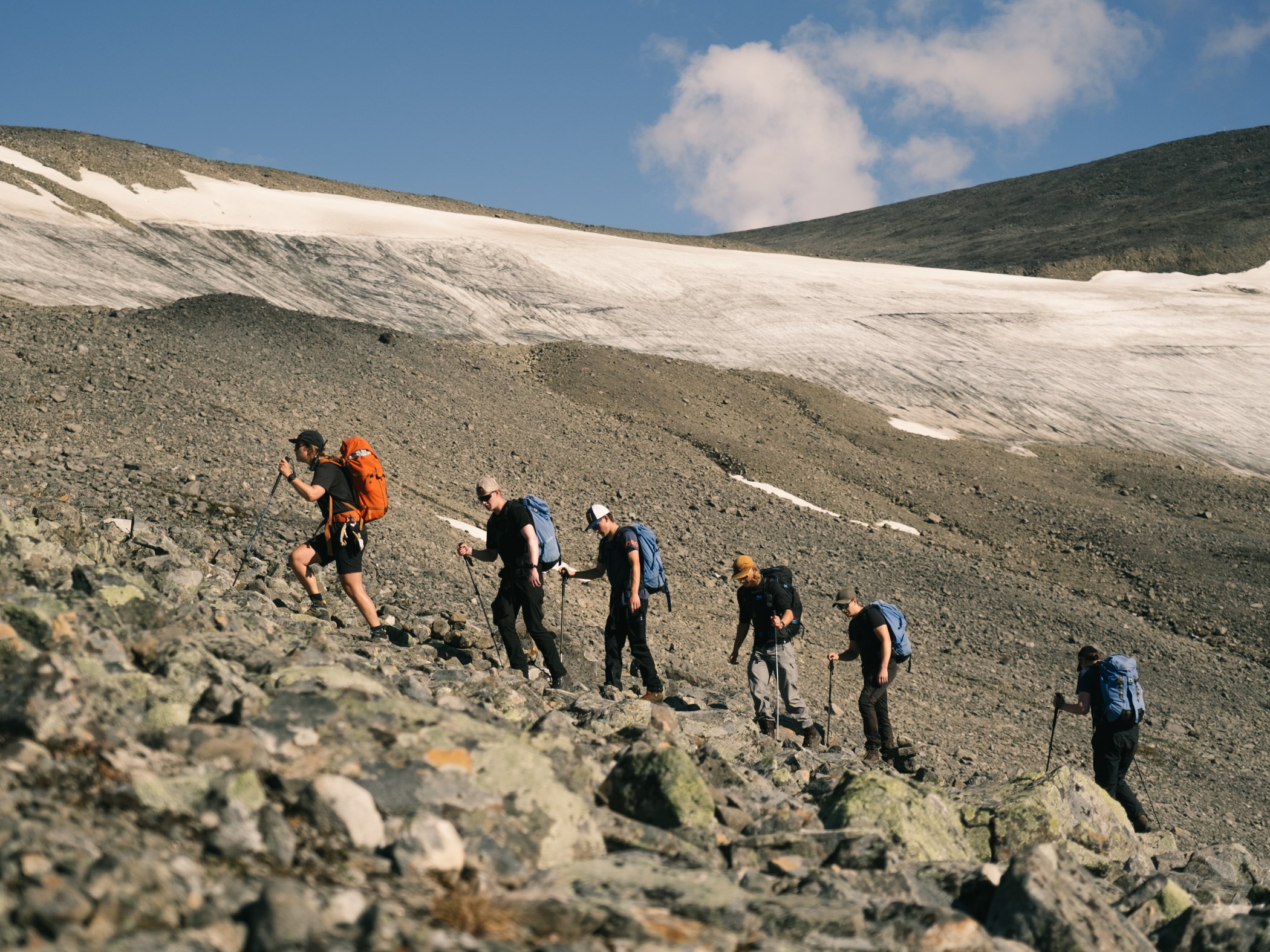 Hikers ascending rocky terrain beside a glacier.