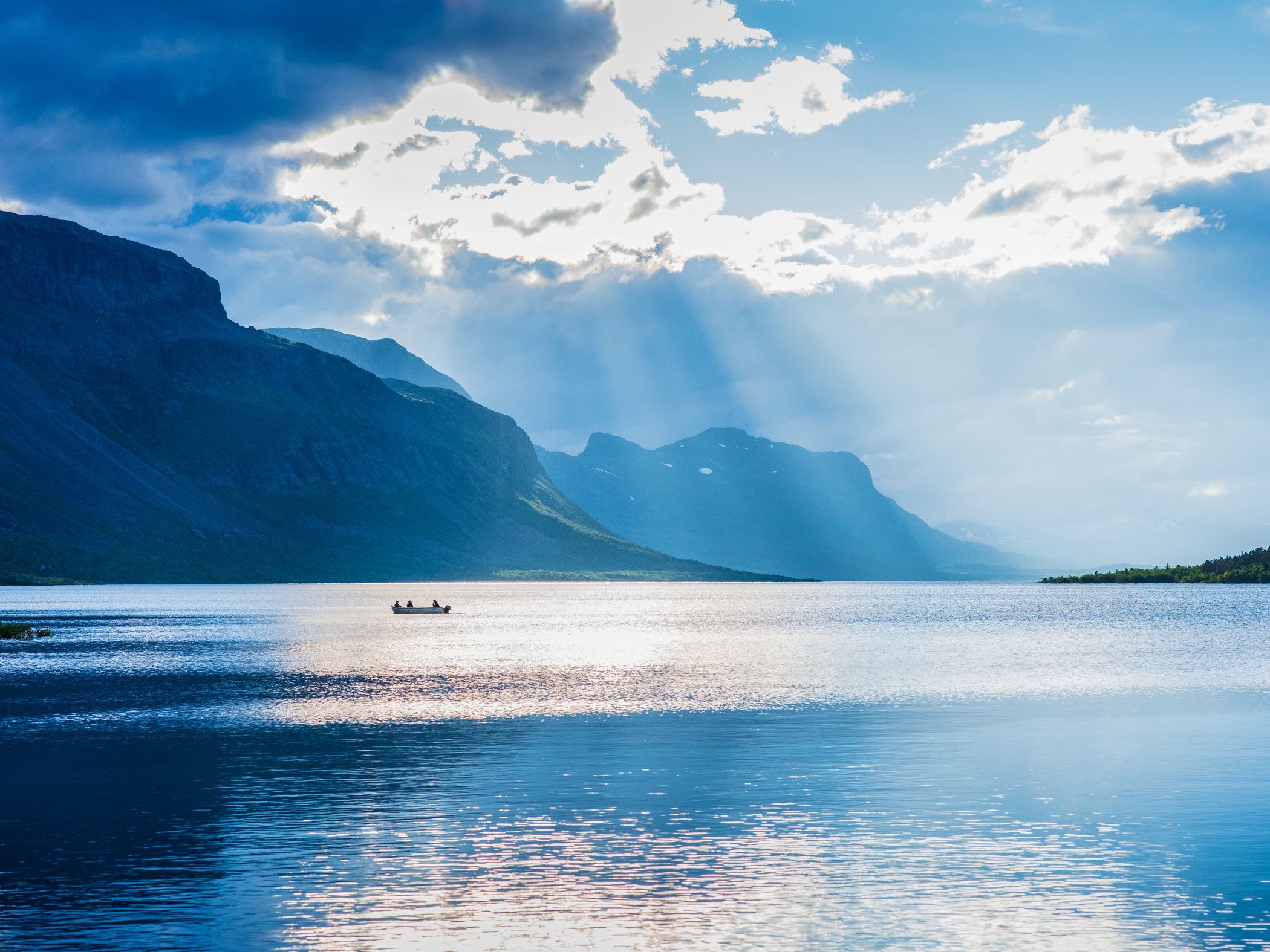 Sunrays breaking through clouds above a mountain lake.