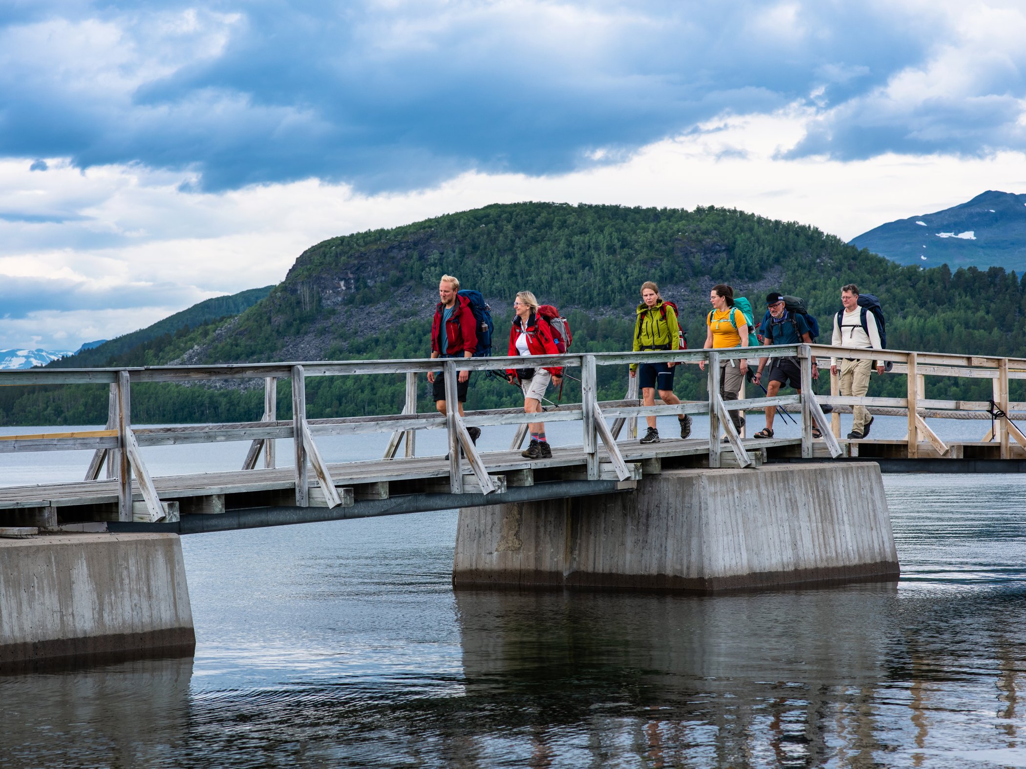 Hikers crossing a bridge over a mountain lake.