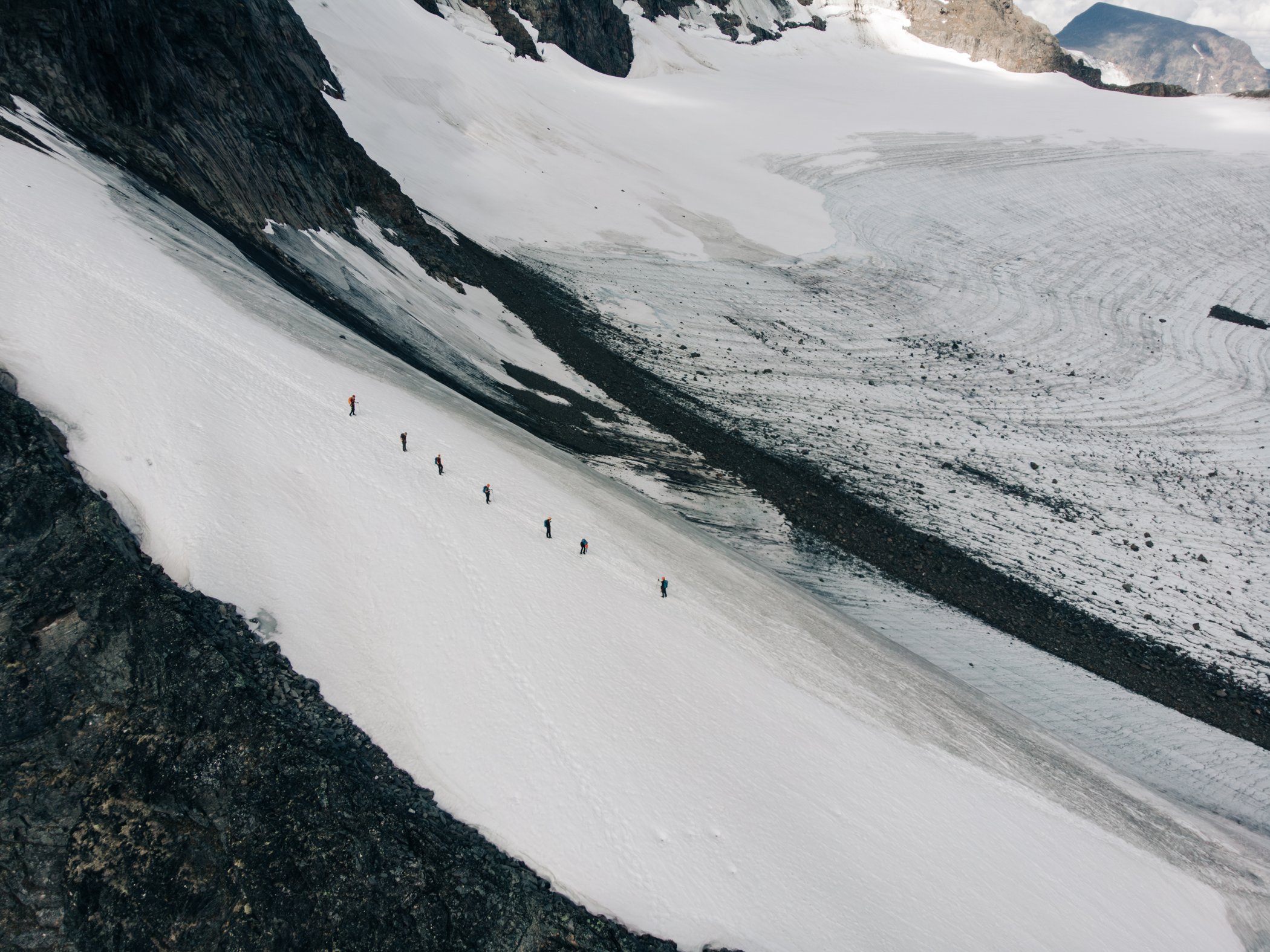 People crossing a glacier in a mountain landscape.
