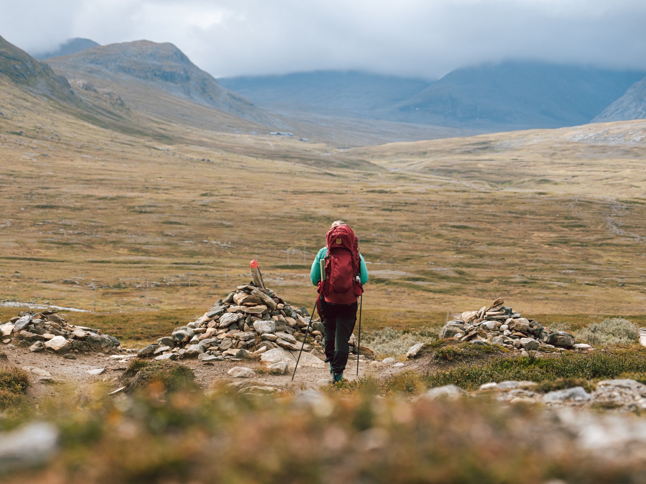 Hiker walking along a mountain trail through a wide valley.