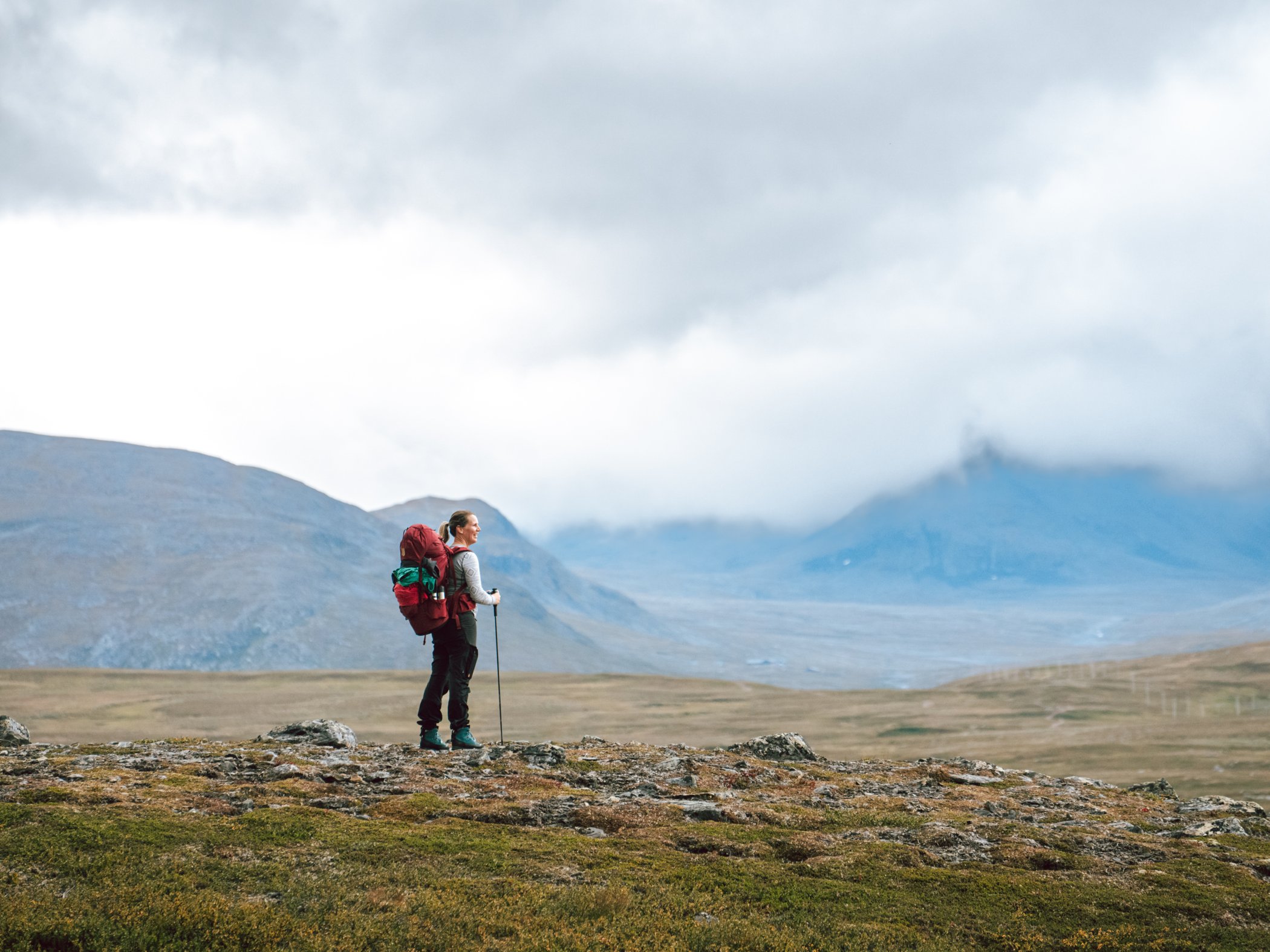 Hiker with a large backpack on an open mountain plateau beneath low clouds.