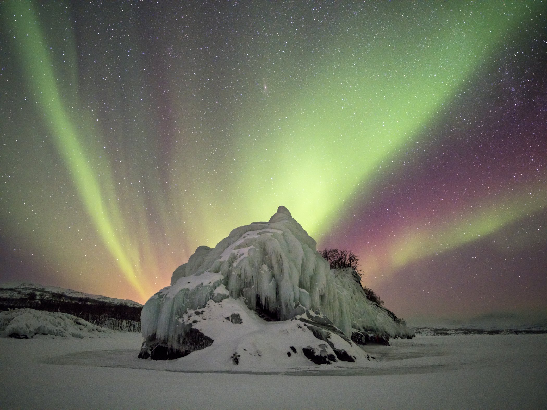 Frozen ice formation illuminated by colourful northern lights on a clear winter night in Abisko.