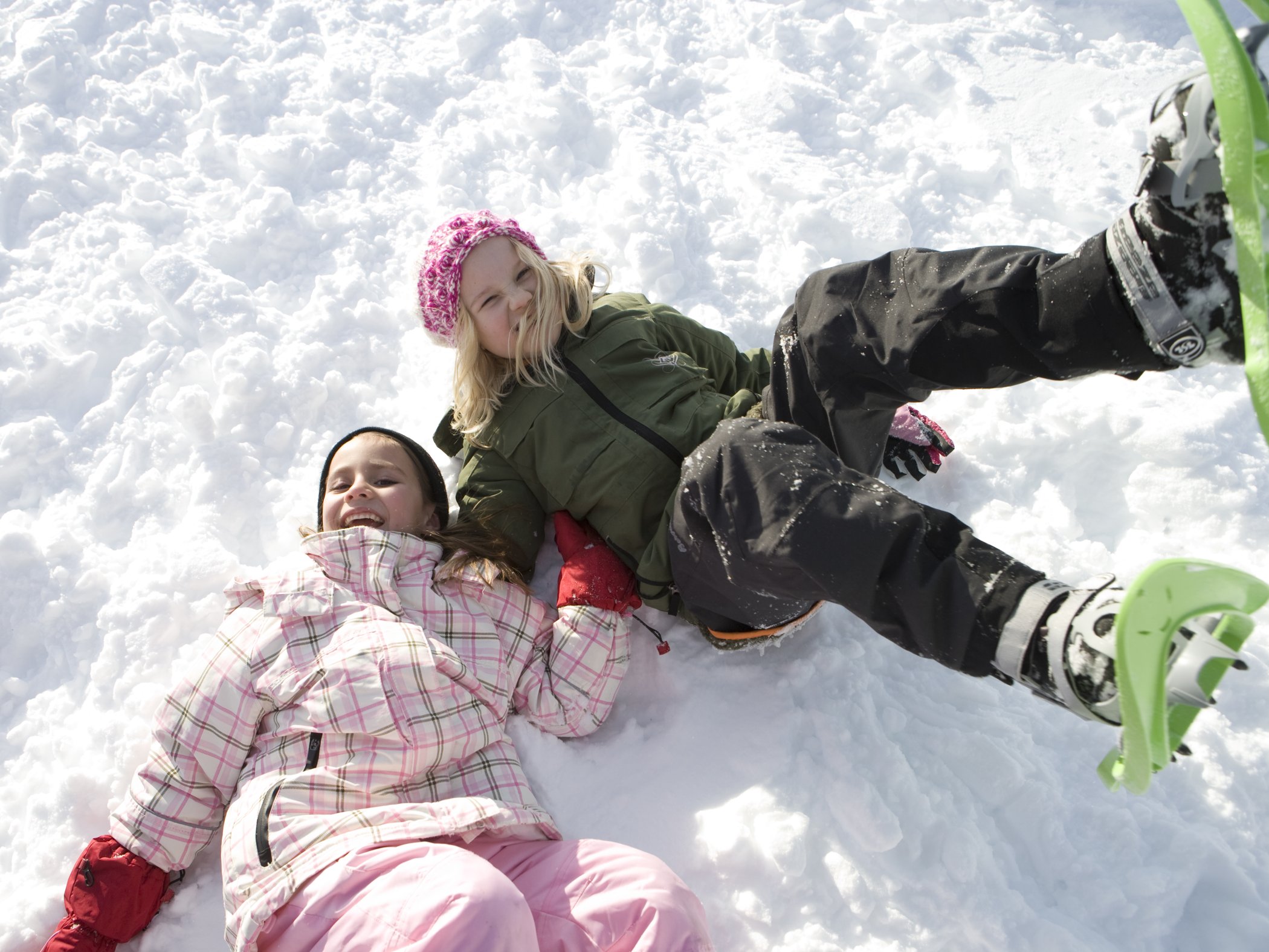 Two children playing in the snow on a winter day, one wearing snowshoes.