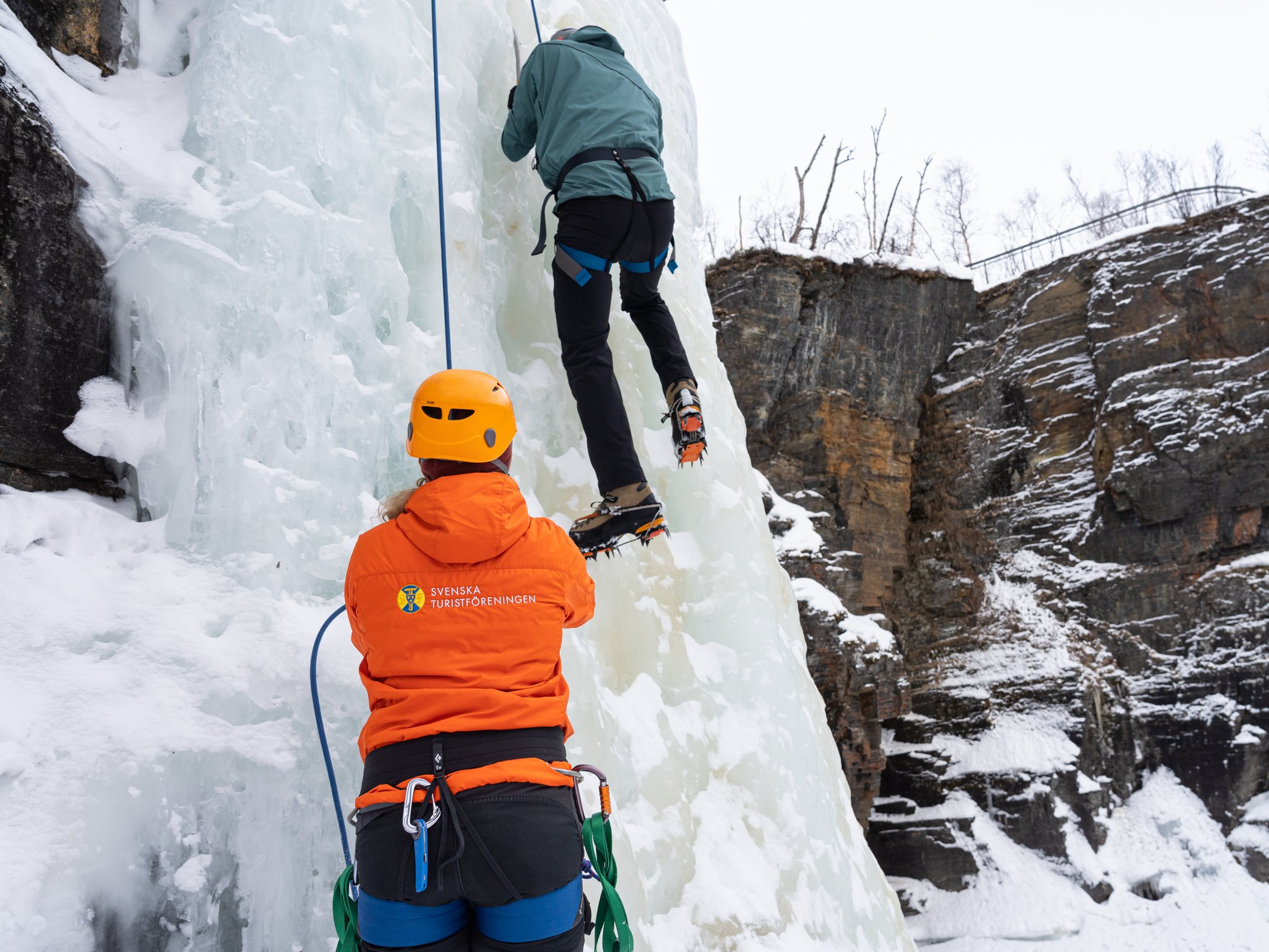 Guide belays a climber on a frozen ice wall during ice climbing in Abisko.