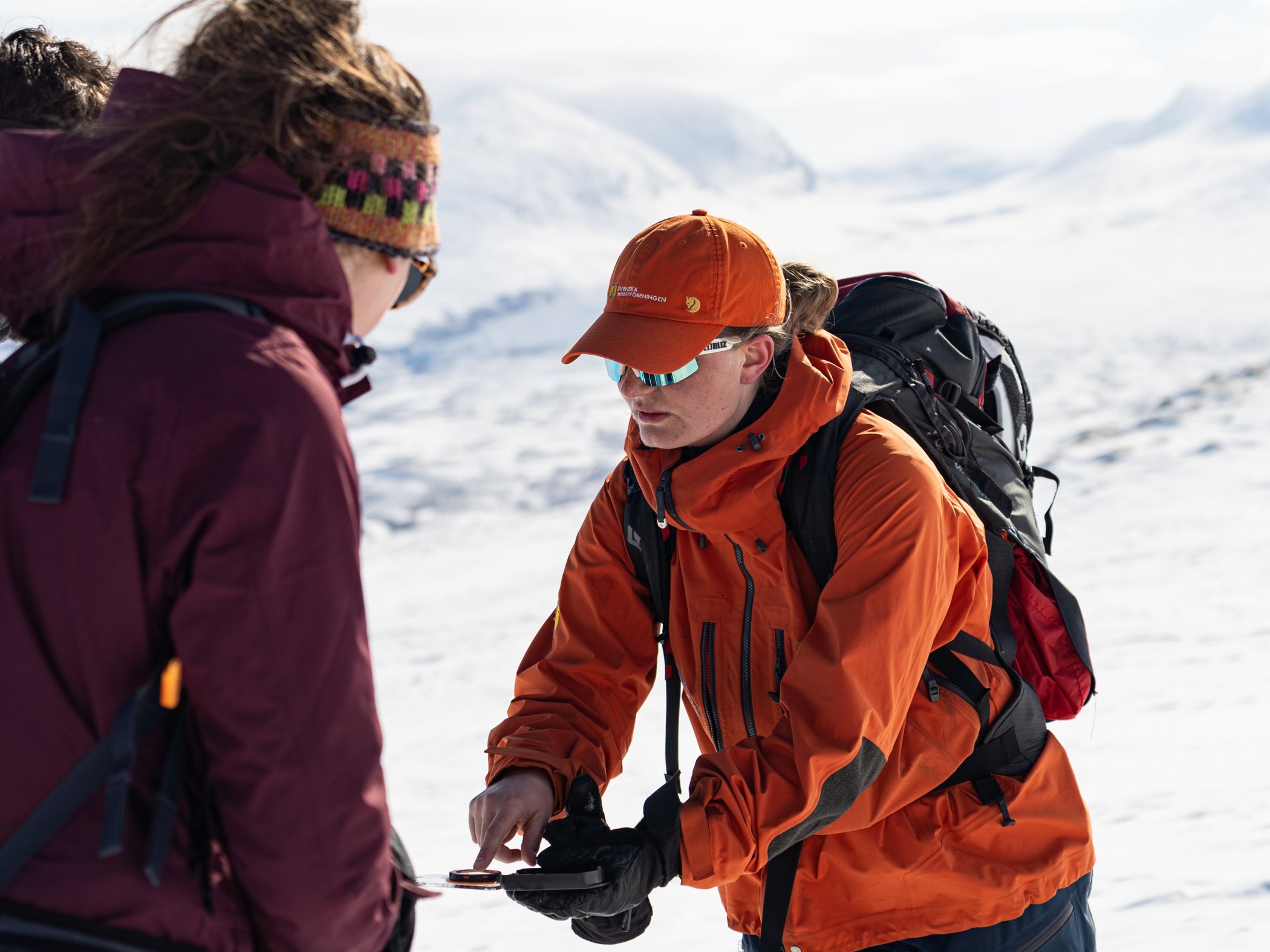 Mountain guide showing a route on a map during a winter expedition in a snow-covered mountain landscape.