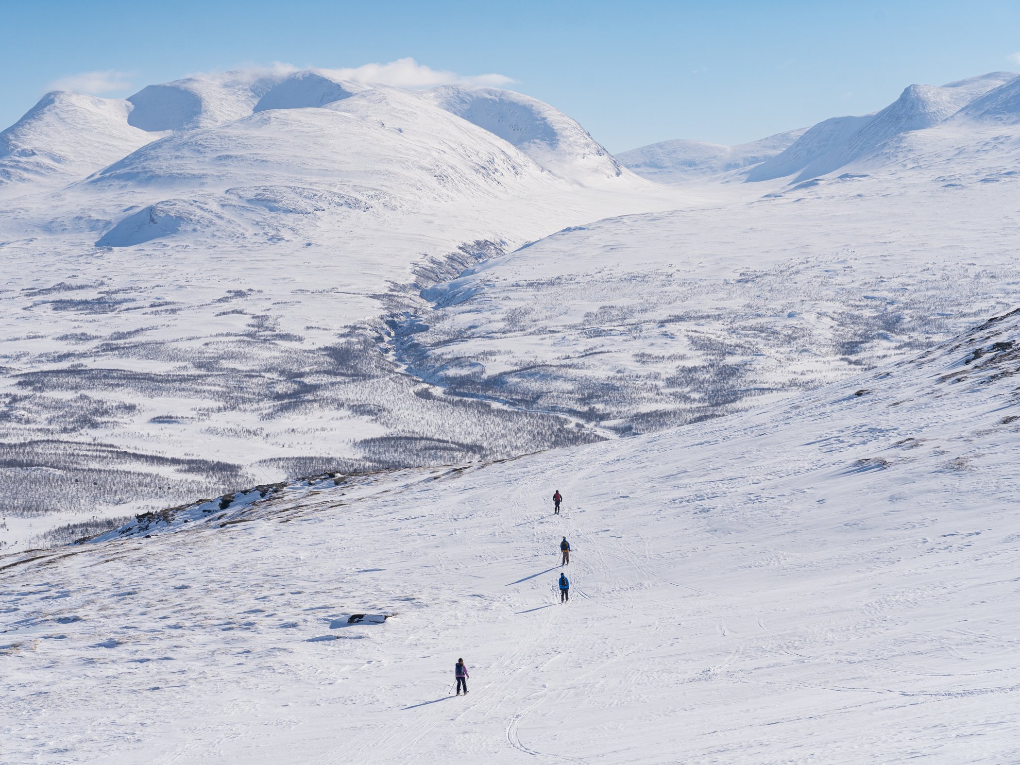 Ski tourers travel through the open mountain landscape during a ski touring excursion in Abisko.